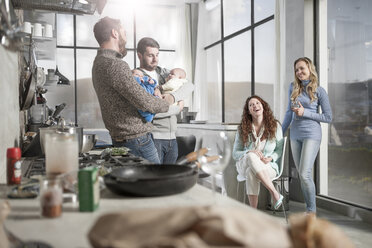 Two wives watching husbands holding their babies in kitchen - ZEF14439