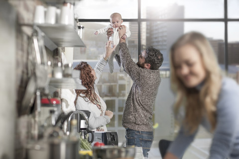 Mann und Frau heben Baby in der Küche hoch, Frau im Vordergrund, lizenzfreies Stockfoto