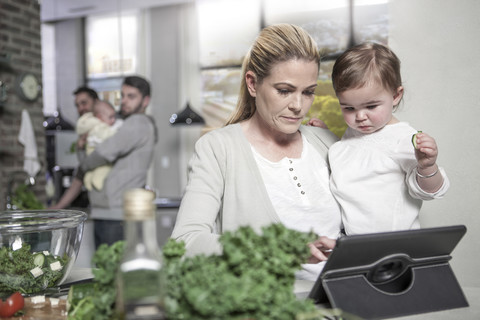Mutter hält Baby mit Tablet in der Küche, lizenzfreies Stockfoto
