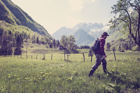 Slovenia, Bovec, angler walking on meadow towards Soca river - BMAF00336