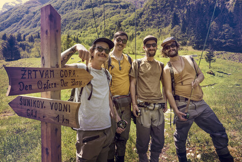 Slovenia, Bovec, four anglers posing at signpost on meadow near Soca river - BMAF00340