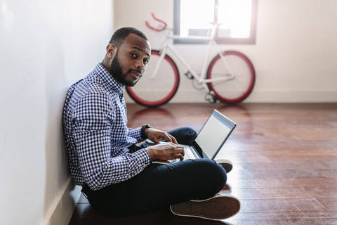 Man using laptop sitting on wooden floor with bicycle in background stock photo