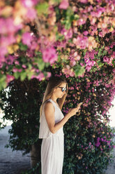 Frau benutzt Mobiltelefon im Park unter rosa Blüten - JPF00275