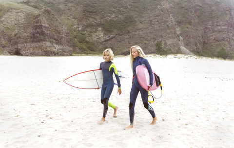 Spanien, Aviles, zwei junge Surfer gehen am Strand spazieren, lizenzfreies Stockfoto