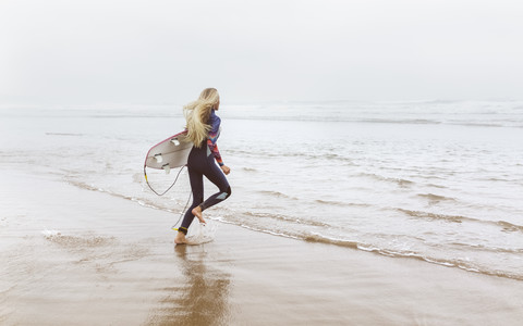 Spanien, Aviles, junger Surfer läuft zum Wasser, lizenzfreies Stockfoto