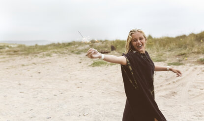 Spanien, Aviles, glückliches Teenager-Mädchen mit einer Wunderkerze am Strand - MGOF03568