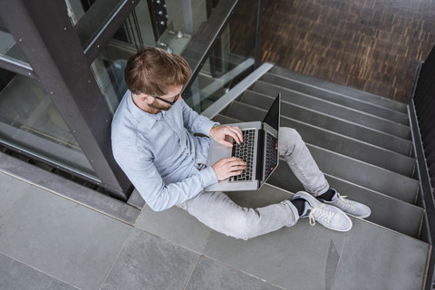 Mann mit Laptop auf einer Treppe im Büro sitzend, lizenzfreies Stockfoto