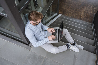 Man using laptop sitting on stairs in office - DIGF02720