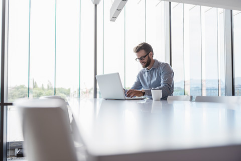 Mann mit Laptop sitzt am Konferenztisch im Büro, lizenzfreies Stockfoto