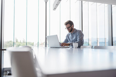 Man using laptop sitting at conference table in office - DIGF02723