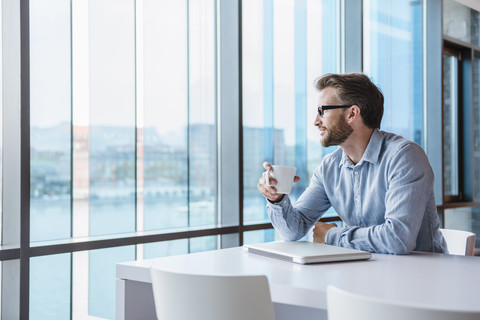 Mann mit Laptop und Kaffeetasse in einem modernen Bürogebäude sitzend, lizenzfreies Stockfoto