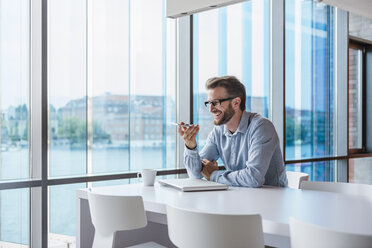 Smiling man using cell phone in modern office - DIGF02729