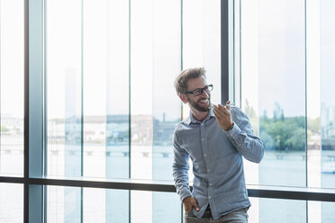 Smiling man using cell phone at the window - DIGF02730