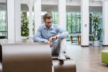 Smiling man checking the time in modern office - DIGF02731