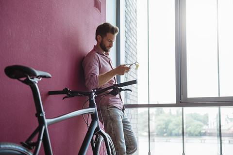 Man with bicycle standing in modern office looking at cell phone stock photo