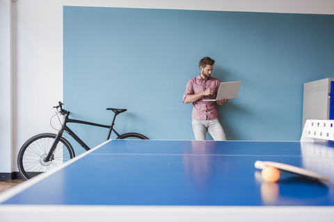 Mann benutzt Laptop im Pausenraum eines modernen Büros, lizenzfreies Stockfoto