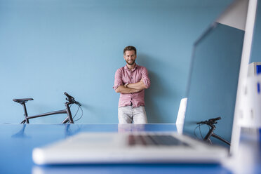 Porträt eines lächelnden Mannes mit Laptop im Pausenraum eines modernen Büros - DIGF02758
