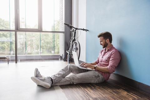 Mann mit Laptop auf dem Boden sitzend im Büro, lizenzfreies Stockfoto