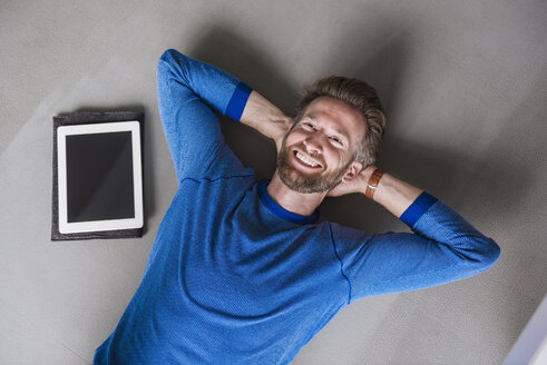 Lächelnder Mann, der neben einem Tablet auf dem Boden liegt - DIGF02762