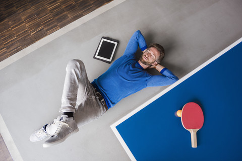 Mann auf dem Boden liegend mit Tablet im Pausenraum eines modernen Büros, lizenzfreies Stockfoto