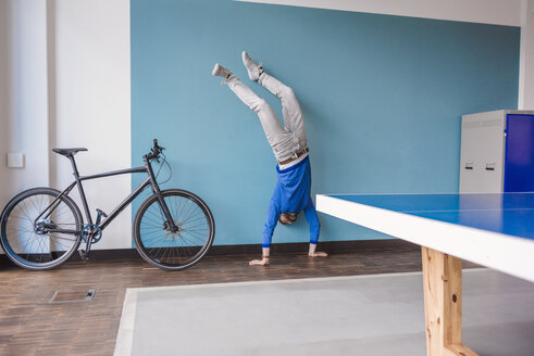 Man doing a handstand in break room of modern office - DIGF02764