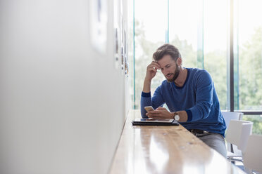 Mann schaut auf Handy auf Tisch am Fenster - DIGF02766