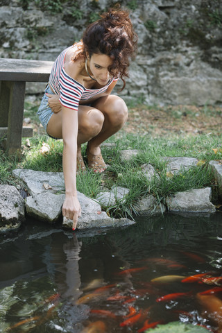 Frau hockt an einem Teich in einem Park, lizenzfreies Stockfoto