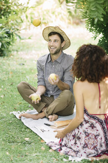 Glückliches Paar beim Picknick im Park mit einem Mann, der mit Äpfeln jongliert - ALBF00171