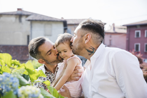 Schwules Paar küsst seine Tochter im Garten, lizenzfreies Stockfoto