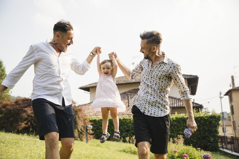 Happy gay couple playing with their child in the garden stock photo