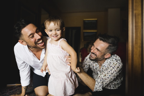 Glückliches schwules Paar spielt mit seiner kleinen Tochter zu Hause, lizenzfreies Stockfoto