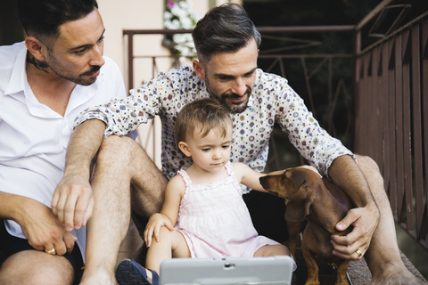 Gay couple with daughter and dog on balcony using digital tablet stock photo