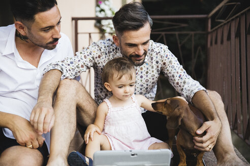 Gay couple with daughter and dog on balcony using digital tablet - MRAF00241