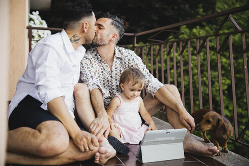 Schwules Paar küsst sich mit Tochter und Hund auf dem Balkon - MRAF00242