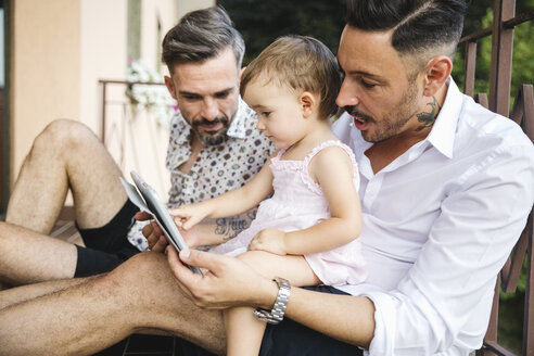 Gay couple with daughter on balcony using digital tablet - MRAF00245
