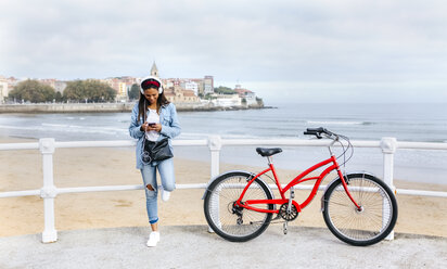 Spanien, Gijon, junge Frau mit Mobiltelefon und Kopfhörern an der Uferpromenade - MGOF03571