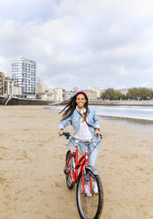 Spanien, Gijon, junge Frau fährt mit dem Fahrrad am Strand - MGOF03573