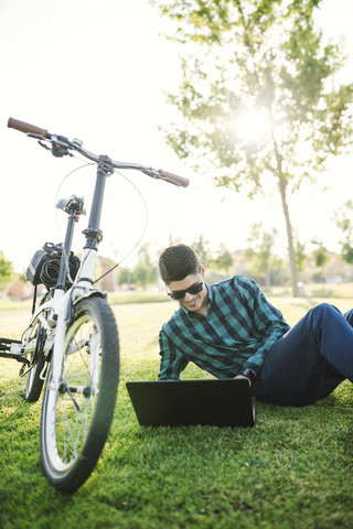 Junger Mann mit Fahrrad und Laptop in einem Park, lizenzfreies Stockfoto