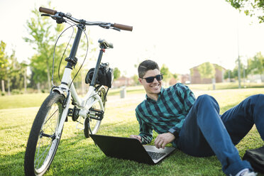 Young man with bicycle using laptop in a park - RAEF01906