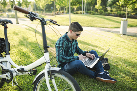 Young man with bicycle using laptop in a park stock photo