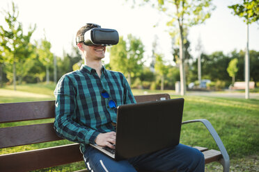 Young man working with VR glasses and laptop on park bench - RAEF01914