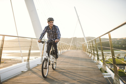 Junger Mann fährt Fahrrad auf einer Brücke bei Sonnenuntergang, lizenzfreies Stockfoto