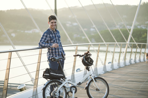 Porträt eines lächelnden jungen Mannes mit Klapprad auf einer Brücke, lizenzfreies Stockfoto