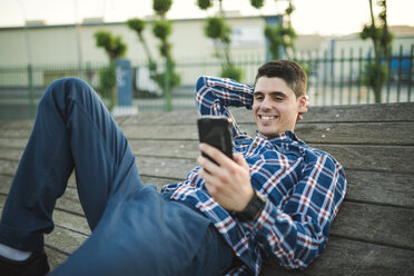 Junger Mann liegt und schreibt eine SMS mit seinem Smartphone - RAEF01924