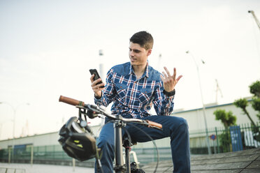 Young man with bicycle looking at smartphone and gesturing - RAEF01926