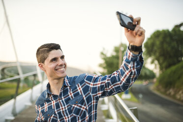 Lächelnder junger Mann macht ein Selfie im Freien - RAEF01931