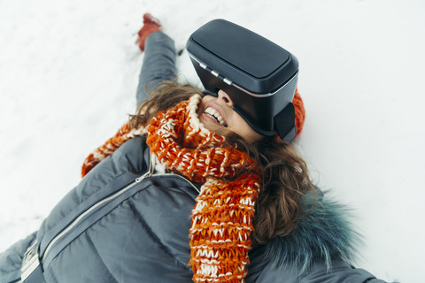 Frau liegt im Schnee und trägt eine Virtual-Reality-Brille, lizenzfreies Stockfoto