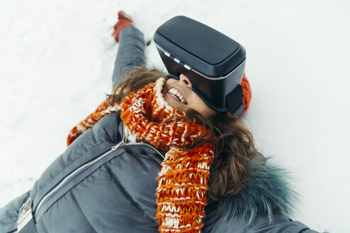 Frau liegt im Schnee und trägt eine Virtual-Reality-Brille - ZEDF00812