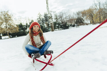 Smiling woman sitting on sledge - ZEDF00820