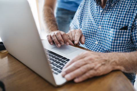Adult grandson teaching his grandfather to use laptop, close-up stock photo